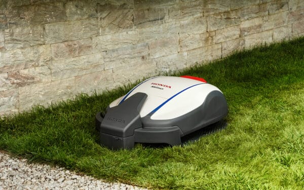 Honda Miimo robotgräsklippare står i sin laddstation på en grön gräsmatta bredvid en mur och en grusgång