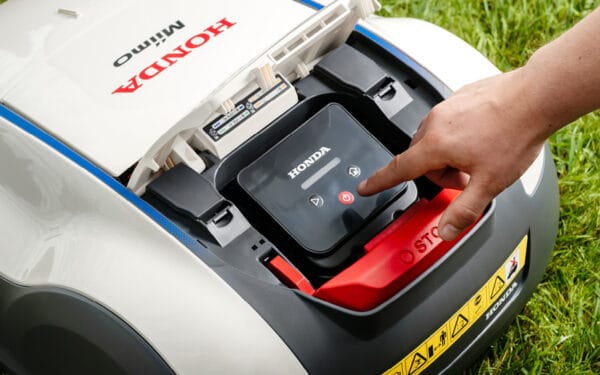 Displayen på en Honda Miimo robotgräsklippare, där en hand pekar på en startknapp