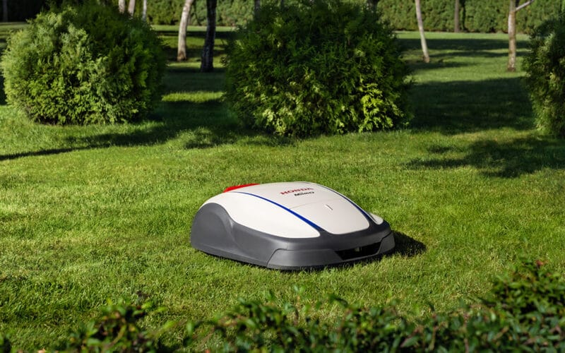 Honda Miimo robotgräsklippare på en grön gräsmatta med en fin grön trädgård i bakgunden