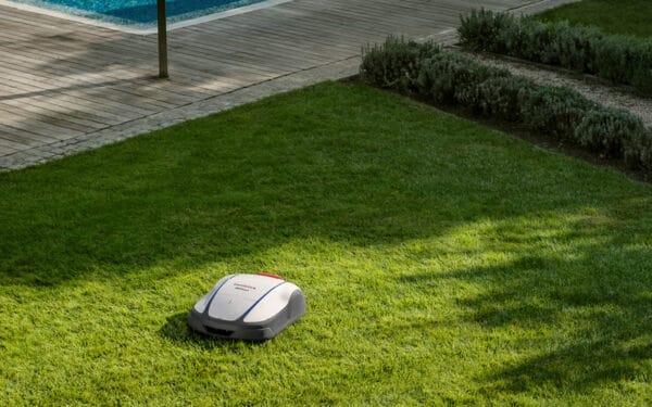 Honda Miimo robotgräsklippare klipper en grön gräsmatta bredvid ett trädäck och en pool