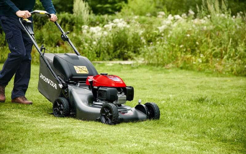 Person kör en gräsklippare från Honda, HRN536 VKEA, i en grönskande trädgård