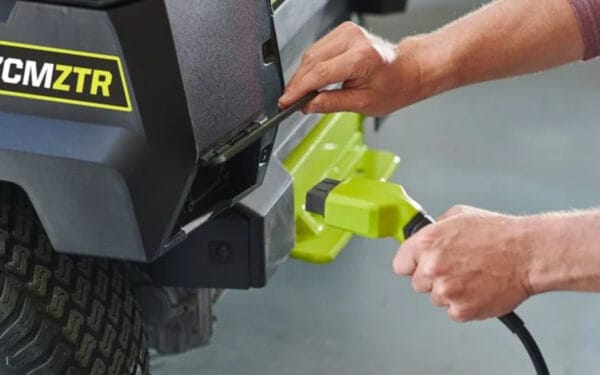 Närbild på en RYOBI åkgräsklippare RY72ZTRX137-310 där två händer stoppar in en laddsladd