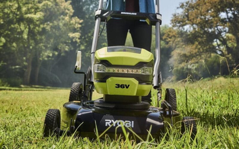 En person som kör en RYOBI gräsklippare RY36LMMX51A_140 på en grön gräsmatta med gröna stora träd i bakgrunden