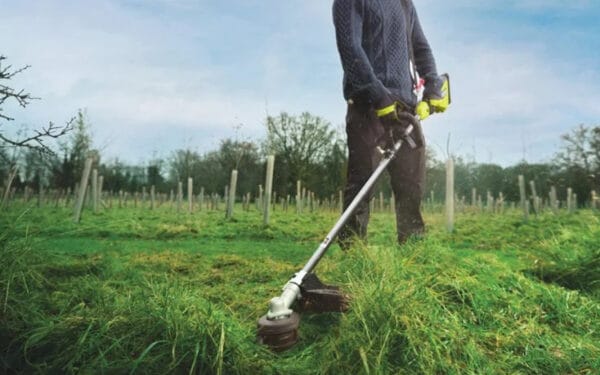 En person håller i en RYOBI grästrimmer RY36LTX40A-0 och klipper gräset