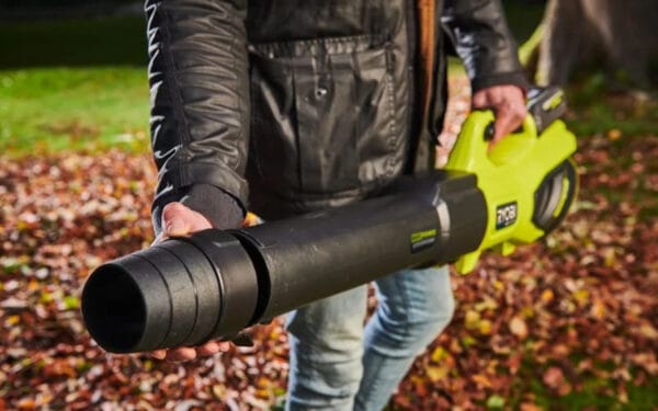 En man håller i en lövblås RY36BLXB-0 från Ryobi med löv och grönt gräs i bakgrunden